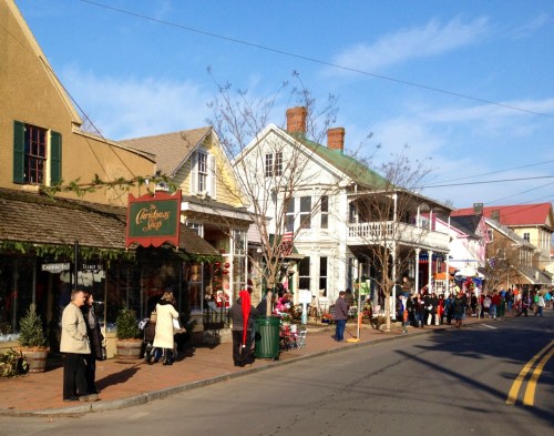 A charming street lined with shops and people, decorated for the holidays under a clear blue sky.