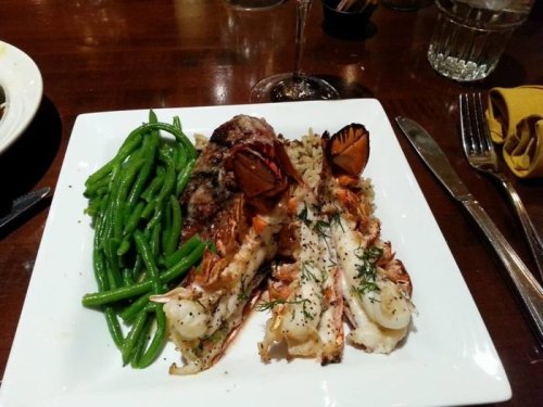 A plate featuring grilled lobster tails, seasoned rice, and green beans on a wooden table.