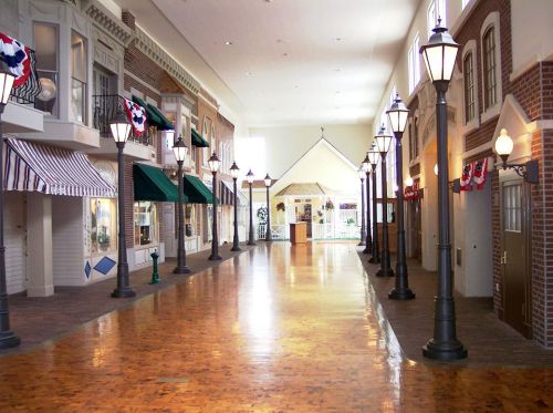 A spacious indoor walkway lined with decorative storefronts and vintage-style street lamps.