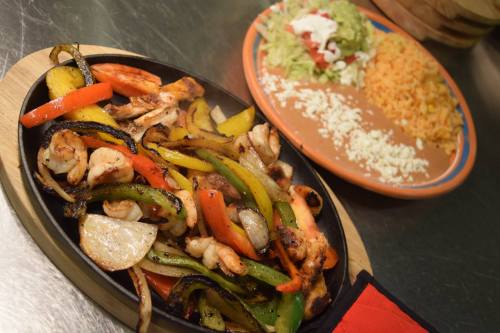Sizzling fajitas with grilled chicken and colorful peppers, served with rice, salad, and cheese on the side.
