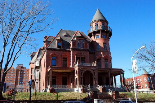 A large, historic red brick mansion with a turret, set against a clear blue sky.