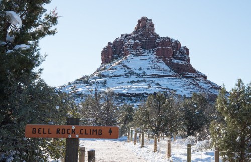 A snowy landscape with a sign for "Bell Rock Climb" and a prominent red rock formation in the background.