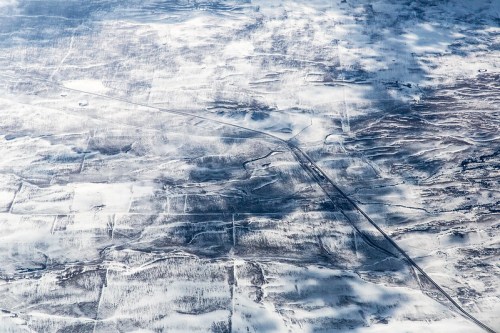 Aerial view of a snowy landscape with winding roads and fields, showcasing a serene winter scene.