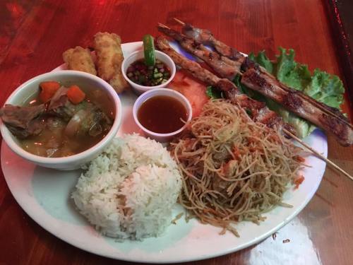 A plate of assorted dishes including rice, noodles, skewers, spring rolls, and a bowl of soup with vegetables.