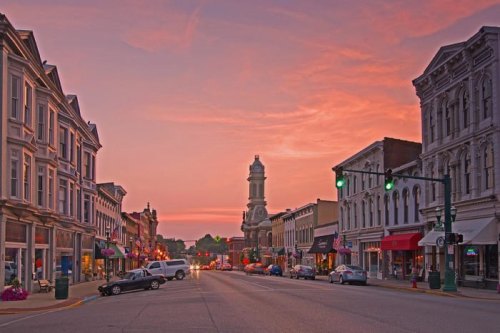 A charming small town street at sunset, featuring historic buildings and a clock tower in the background.