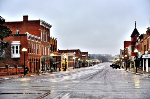 A quiet, rainy street scene in a small town, featuring brick buildings and empty sidewalks.