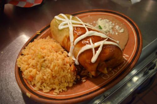 A plate with a burrito topped with sauce and sour cream, served with rice and refried beans.