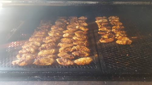 Grilled chicken pieces cooking on a large smoker, surrounded by smoke and heat.