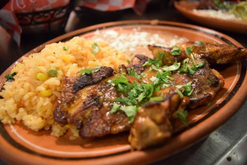 A plate of grilled chicken topped with cilantro, served with rice and corn on the side.