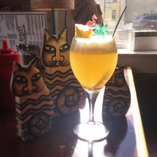 A tropical drink in a glass with a garnish, surrounded by three wooden cat figurines.