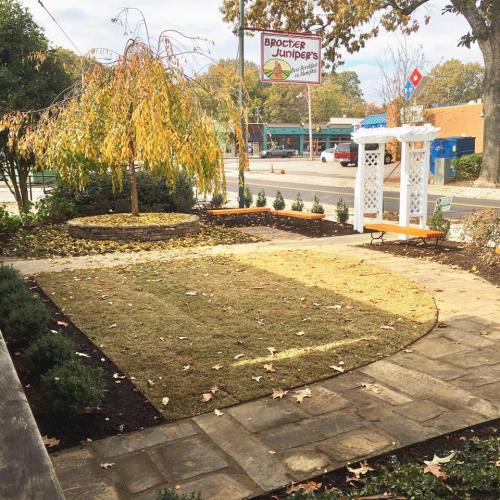 A landscaped area with a circular garden, a weeping tree, and a white gazebo, surrounded by autumn leaves.