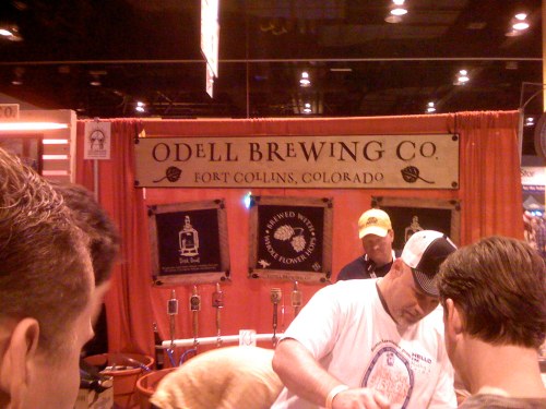 A brewery booth with a sign for Odell Brewing Co., featuring taps and people interacting at a beer festival.