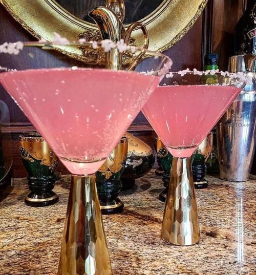 Two pink cocktails in elegant glasses with gold bases, garnished with salt, set on a marble countertop.