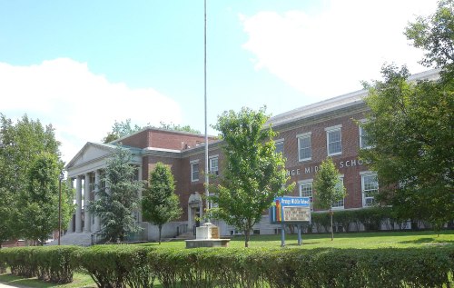 Exterior view of Orange Middle School, featuring brick architecture, trees, and a flagpole on a sunny day.