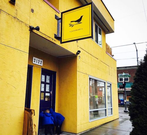 A bright yellow building with a sign reading "Junebarry" and two children in blue jackets near the entrance.