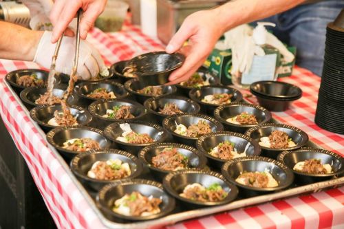 Hands serving portions of food into small black bowls on a checkered tablecloth.
