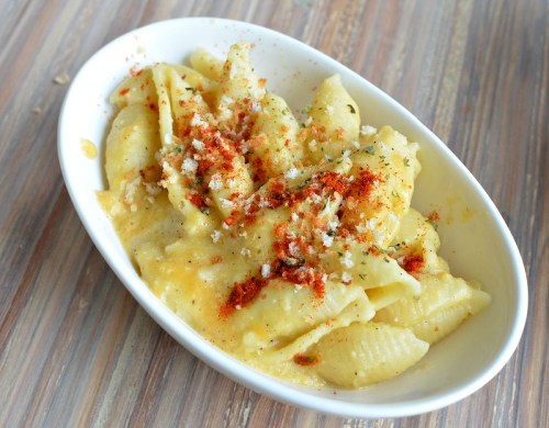 Creamy pasta shells topped with breadcrumbs and spices, served in a white dish on a wooden table.