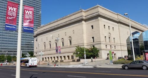 Historic building with ornate architecture, surrounded by modern cityscape and banners welcoming visitors to Cleveland.
