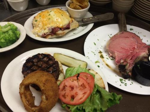 A tray with a prime rib, a burger with lettuce and tomato, onion rings, and a side of broccoli.