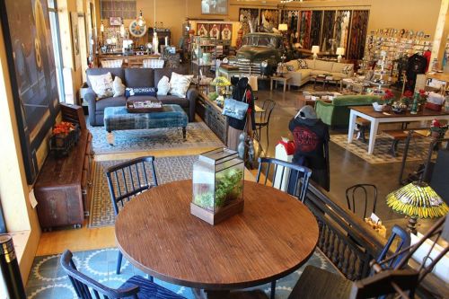 A cozy interior of a home goods store featuring furniture, decor, and a vintage car in the background.