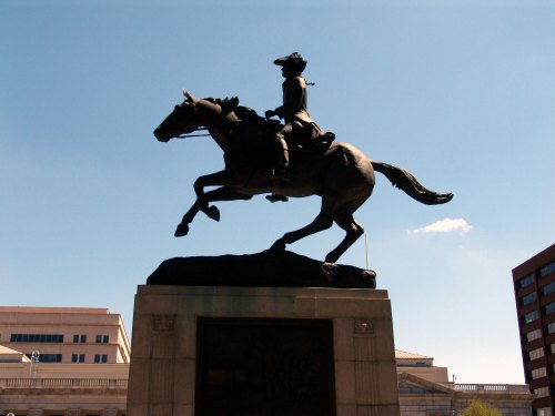 A silhouette of a mounted statue of a soldier on horseback against a clear blue sky.