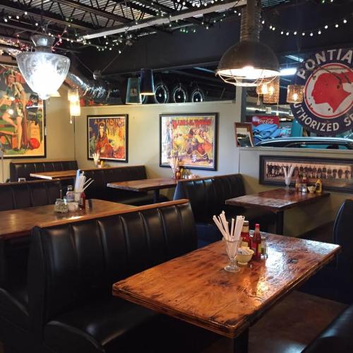 Cozy restaurant interior with wooden tables, black booths, and colorful vintage posters on the walls.