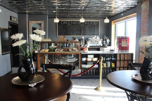 A cozy café interior featuring a counter with a menu, tables with flowers, and a warm, inviting atmosphere.