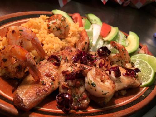 A colorful plate featuring grilled shrimp, rice, avocado, and fresh vegetables, garnished with lime and herbs.