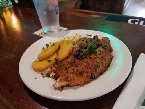 A plate of seasoned fish fillet with coleslaw and fried cornmeal cakes, garnished with parsley.