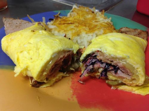 A colorful plate featuring a folded omelet with ham and coleslaw, alongside crispy hash browns and toast.