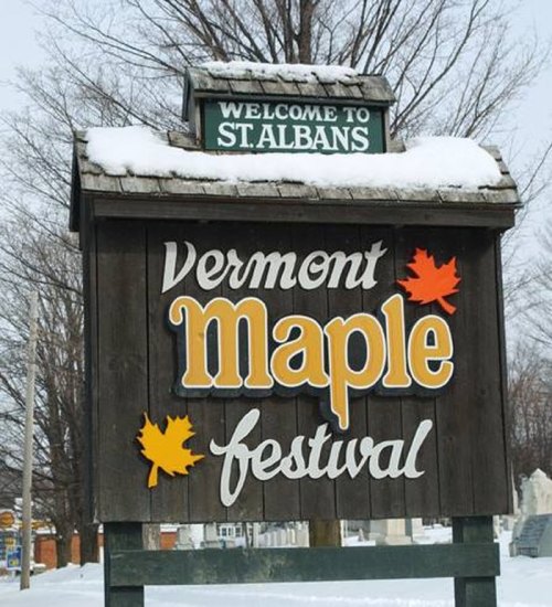 Welcome sign for St. Albans, Vermont, featuring the Vermont Maple Festival with snow-covered trees in the background.
