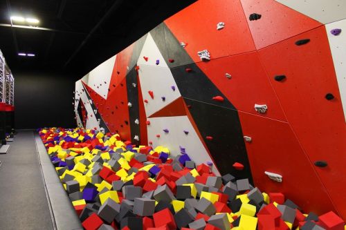 A colorful indoor climbing gym featuring a bouldering wall and a large pit filled with foam blocks.
