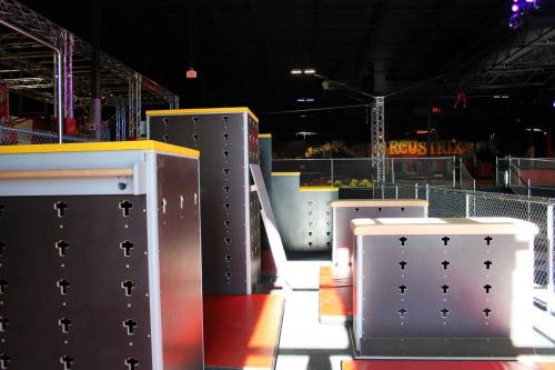 Indoor obstacle course with various climbing structures and platforms, brightly lit in a recreational space.
