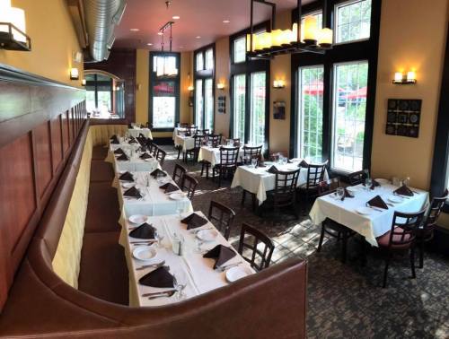 A spacious restaurant interior with neatly set tables, white tablecloths, and large windows letting in natural light.