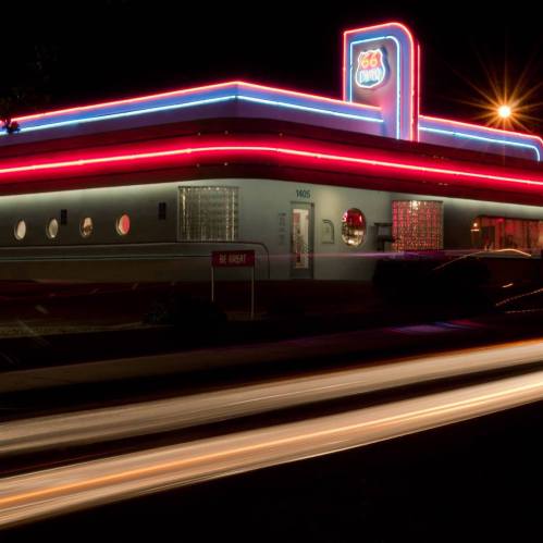 A retro diner illuminated with neon lights at night, featuring circular windows and a glowing sign.
