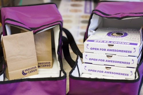 Two purple bags open to reveal cookie boxes and a brown paper bag labeled "Precious Cargo."