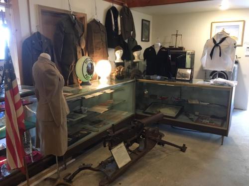 Display of historical military uniforms and artifacts in a museum setting, featuring a vintage machine gun and memorabilia.