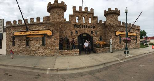 A stone castle-shaped building with towers, featuring signs for a playground and attractions, on a city street.