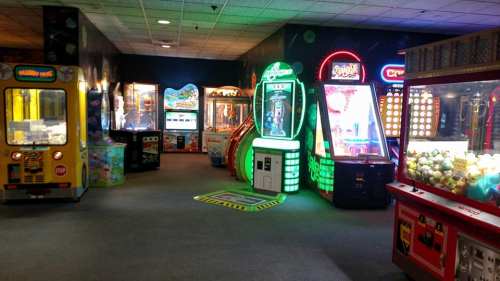 A vibrant arcade filled with various colorful game machines and attractions, including claw machines and racing games.
