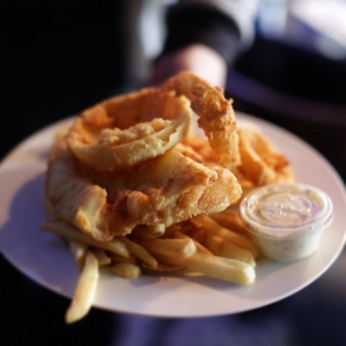 A plate of golden fried fish and chips, served with a small container of dipping sauce.