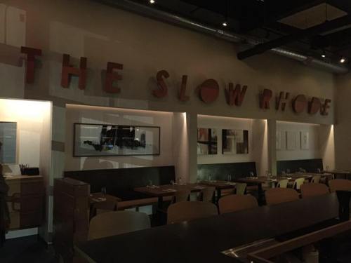 Interior of a restaurant named "The Slow Rhode," featuring modern decor and dim lighting. Tables are set for dining.