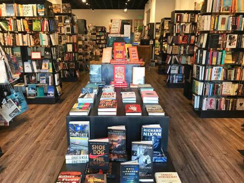 A cozy bookstore interior with shelves of books and a display table featuring various titles in the center.