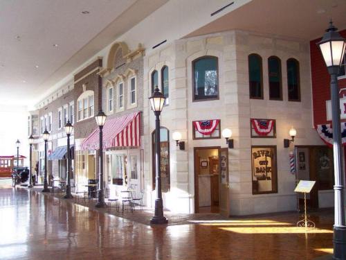 A charming indoor street scene with storefronts, decorative awnings, and vintage-style street lamps.