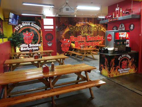 Interior of Rollin Smoke Barbeque featuring wooden tables, a soda machine, and vibrant wall murals.