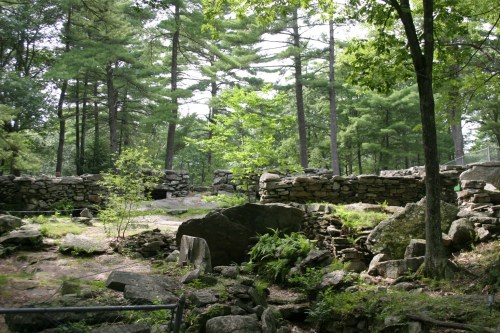 Ruins of stone walls amidst lush green trees and rocky terrain in a forested area.