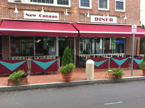 Exterior of New Canaan Diner with red awnings, green accents, and outdoor seating surrounded by potted plants.