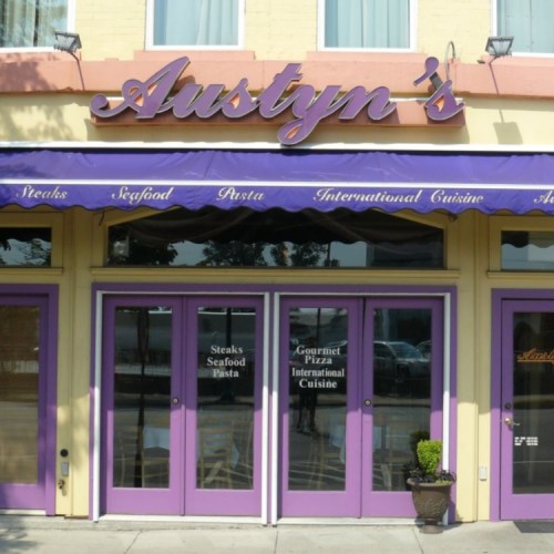 Exterior of Austyn's restaurant featuring a purple awning and doors, with signage for steaks, seafood, and international cuisine.