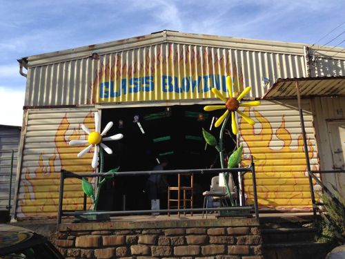 A colorful metal building with a sign reading "Glass Blowing" and large flower decorations on the entrance.