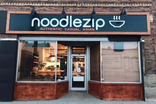 Exterior of Noodlezip restaurant featuring a modern sign and large windows, showcasing a casual Asian dining atmosphere.