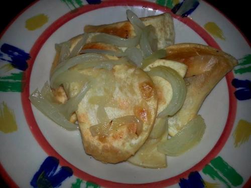 A colorful plate with fried tortillas topped with sautéed onions.